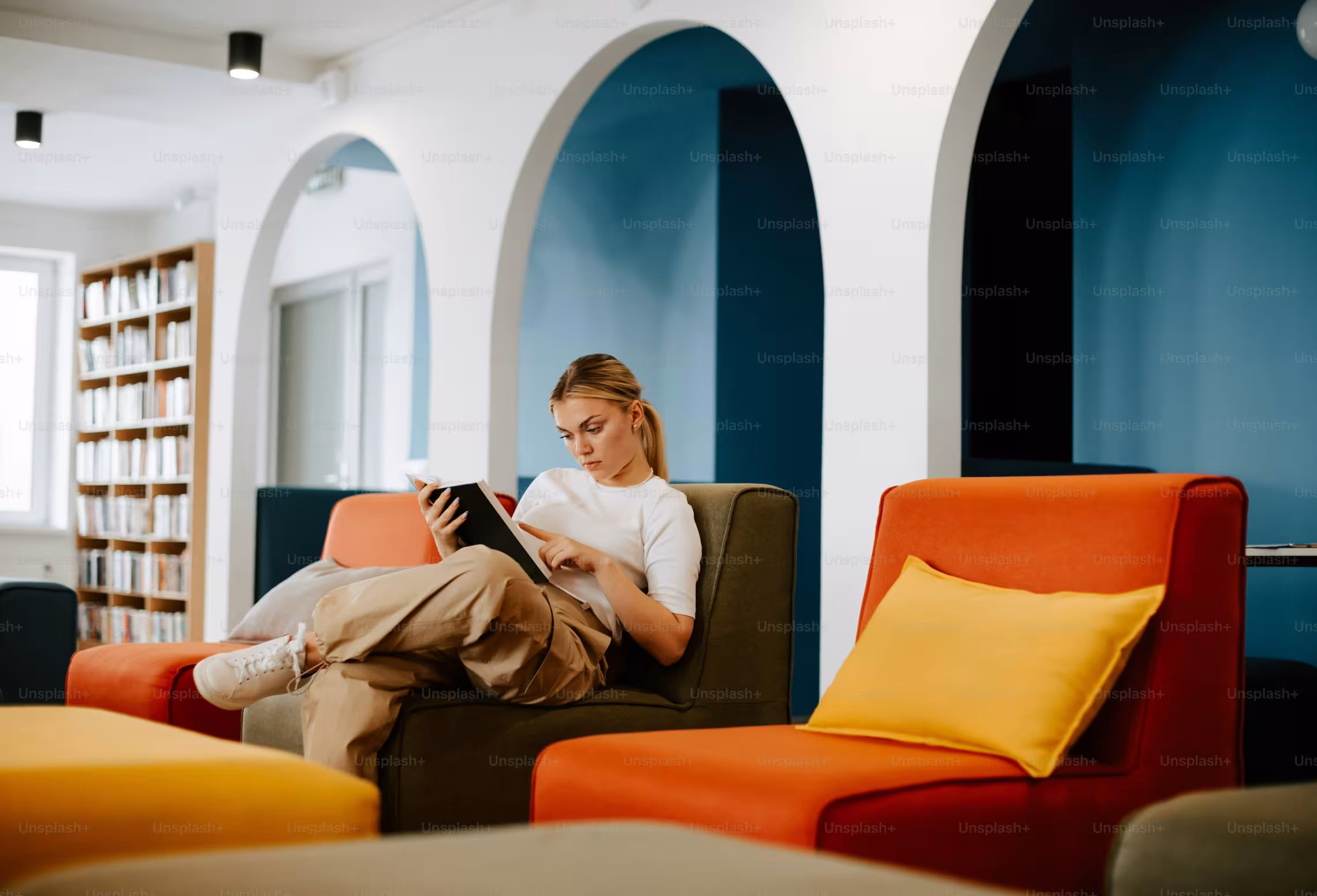 Une étudiante lit un livre dans une bibliothèque moderne.